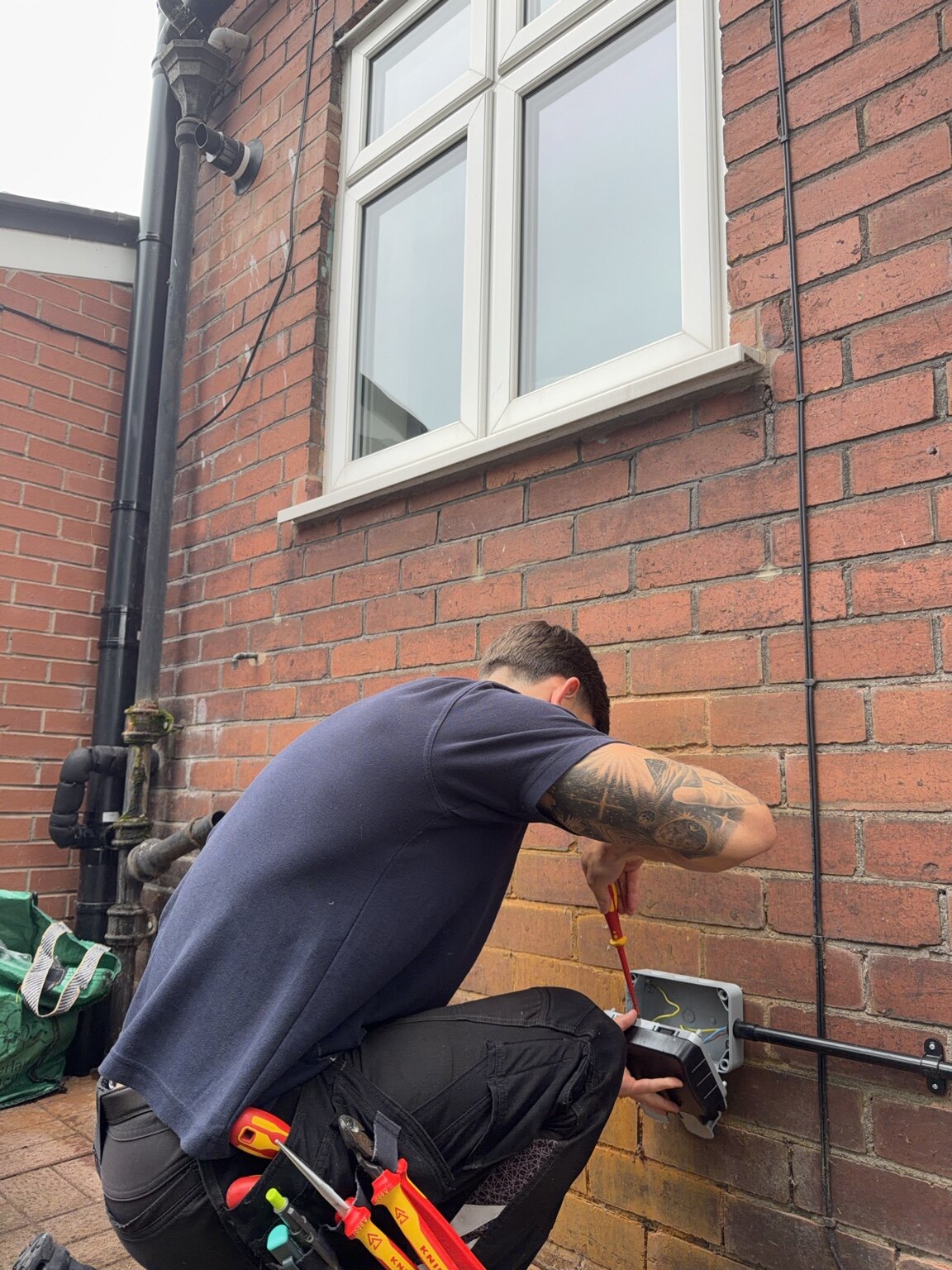 Electrician working on an external electrical enclosure at a brick home